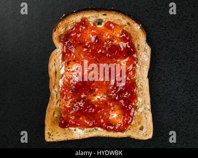 Erdbeer-Marmelade oder Konserve auf Buttertoast vor schwarzem Hintergrund Stockfoto