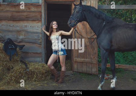 Cowboy-Frau hält ein Pferd durch die Zügel auf dem Bauernhof. Stockfoto