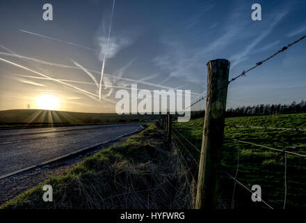 Sonnenuntergang über Landstraße, Jet Spuren am Himmel im Peak District National Park, Derbyshire, Großbritannien. Stockfoto