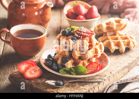 Hausgemachte belgische Waffeln mit Erdbeeren, Heidelbeeren und Sirup, in Platte auf Holztisch Stockfoto