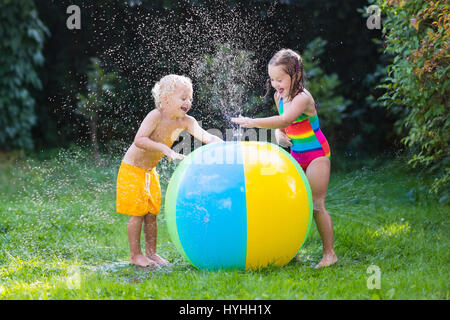 Kind spielt mit Spielzeug Ball Garten Sprinkler. Vorschulkind Kind laufen und springen. Sommer im freien Wasserspaß im Hinterhof. Kinder spielen mit Schlauch Bewässerung Stockfoto