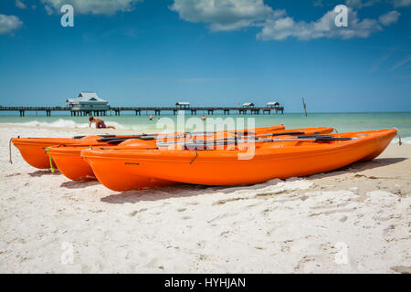 Orange-Kajaks ruhen am weißen Strand von Clearwater Beach, FL, mit Strandbesucher in der Nähe von Pier 60 & Küstenlinie in dieser Süd-West-Urlaubsziel Stockfoto