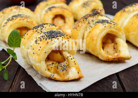 Hausgemachte Croissants (Brötchen) mit Äpfeln, dekoriert mit Mohn auf einem dunklen Hintergrund aus Holz. Stockfoto