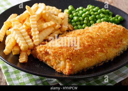 Traditionelle britische Gerichte: Fish And Chips mit grünen Erbsen Nahaufnahme auf einer Platte auf einem Tisch. horizontale Stockfoto