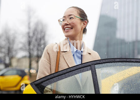 Asiatische Geschäftsfrau mit Taxi in regnerischen Straße Stockfoto