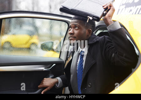 Afrikanische Unternehmer verlassen Taxi in Regen Stockfoto