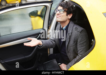 Junger Geschäftsmann verlassen Taxi in Regen Stockfoto