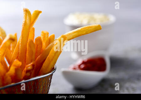 Nahaufnahme von einigen leckeren Pommes frites serviert in einem Metallkorb und einige Schüsseln mit Mayonnaise und Ketchup im Hintergrund auf einem grauen rustikalen Holz Stockfoto