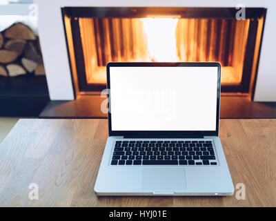 Laptop mit leeren Bildschirm auf Holztisch vor der brennenden Kamin - hot Angebot Konzept Stockfoto