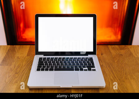 Laptop mit leeren Bildschirm auf Holztisch vor der brennenden Kamin - hot Angebot Konzept Stockfoto