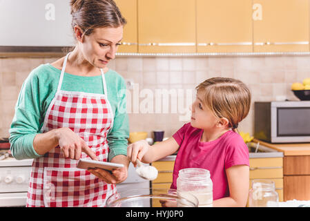 Mutter mit Tablet in der Küche mit Tochter und Pizza Teig Stockfoto