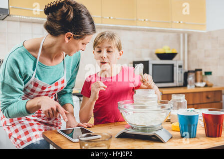 Mutter mit Tablet in der Küche mit Tochter und Pizza Teig Stockfoto