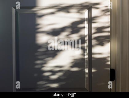 Gefleckte Sonnenlicht schafft abstrakte Schatten auf weiße Tür Stockfoto