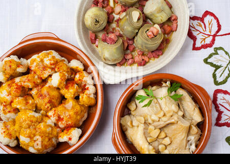 Tapas essen. Traditionelle Gerichte der spanischen Gastronomie. Blumenkohl mit Pimentón, Artischocken mit Schinken und Champignons mit Knoblauch Stockfoto