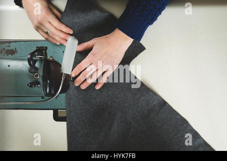 Händen der Schneiderin Nähen mit einer professionellen Maschine einen grauen Stoff. Ansicht von oben Stockfoto