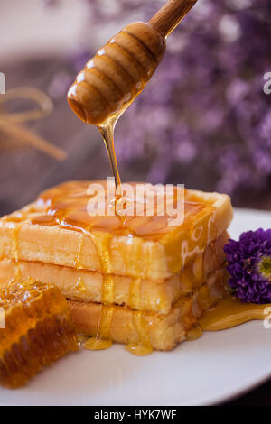 Tropfen Honig aus einem hölzernen Wagen auf gebackene Waffel Stockfoto
