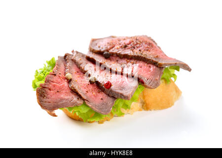 Gebratenes Rinderfilet mit Pfeffer auf einer Scheibe Baguette mit einem Blatt Salat Stockfoto