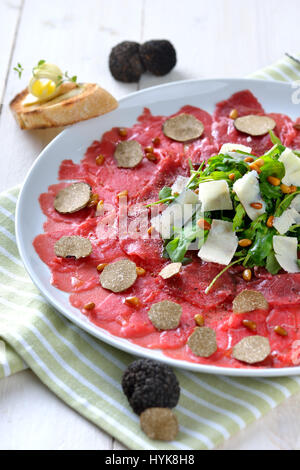 Köstliches Rindfleisch-Carpaccio mit in Scheiben geschnittenen schwarzen Trüffeln, Rucola-Salat mit Parmesan und gerösteten Pinienkernen, serviert mit einer Scheibe geröstetes baguette Stockfoto