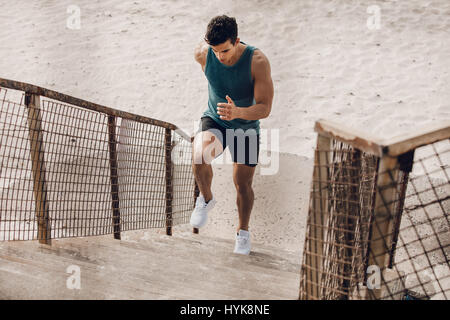 Muskulöser junger Mann auf der Treppe am Strand ausüben. Junge Läufer die Treppenstufen am Strand. Stockfoto