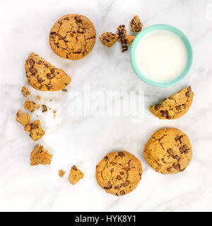 Ein quadratischer Foto der frisch gebackene Schokolade chips Cookies, bilden einen Kreis Rahmen für einen Text oder Logo, mit einem Glas Milch, auf einer weißen Marmor Textur Stockfoto