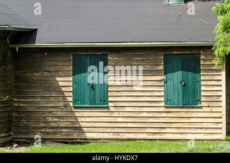 Partielle Seite des rustikalen Bauernhof Gebäude im Blick mit verwitterten Abstellgleis und grünen Fensterläden.  Fotografieren bei vollem Tageslicht. Stockfoto