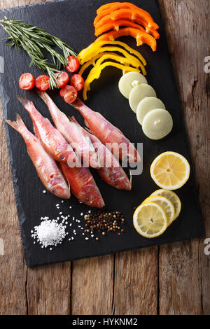 Roher Fisch Rotbarbe mit pflanzlichen Zutaten und Gewürzen close-up auf dem Brett Küche. Vertikale Ansicht von oben Stockfoto