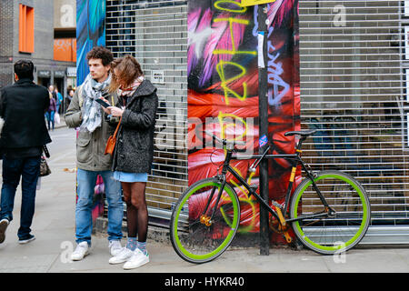 Touristen stehen durch die Wand in Brick Lane, auf der Suche nach dem Weg auf dem Handy Stockfoto