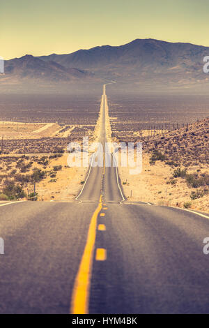 Klassische vertikale Ansicht einer endlosen geraden Straße laufen durch die karge Landschaft des berühmten Death Valley mit extremer Hitze Dunst an einem sonnigen Tag Stockfoto