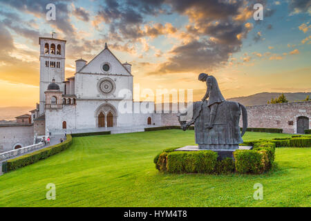 Klassische Ansicht der berühmten Basilika des Heiligen Franziskus von Assisi (Basilica Papale di San Francesco) mit schönen goldenen Abendlicht mit Dramati-statue Stockfoto