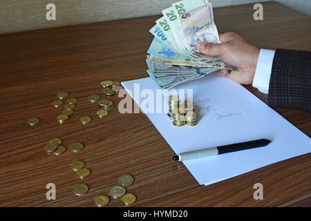 Arm der Unternehmer in Jacke hält Papier-Währungen, Euro, US Dollar und Lira mit Stift und Münze auf Notizpapier Stockfoto