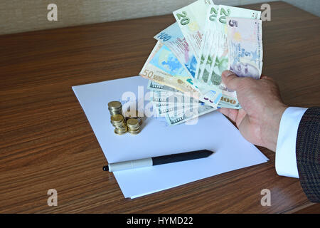 Arm der Unternehmer in Jacke hält Papier-Währungen, Euro, US Dollar und Lira mit Stift und Münze auf Notizpapier Stockfoto