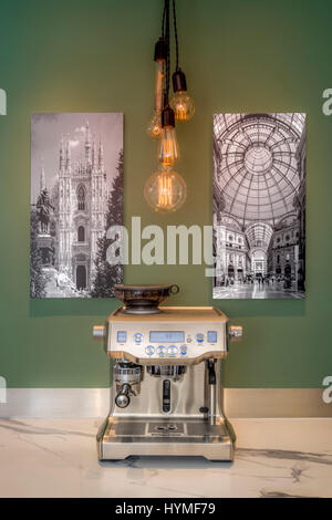 Espresso geben traditionellen Kaffeemaschine auf der Arbeitsplatte in der Küche mit hängenden Retro-Lampen und Fotoabzüge von Mailand an Wand. Stockfoto