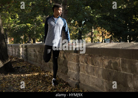 Ein Portrait eines jungen Mannes Dehnung als er bereitet zu erarbeiten. Im Herbst 2016 in Prospect Park in Brooklyn, New York City gedreht. Stockfoto