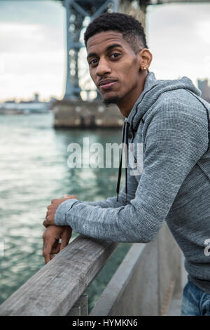 Ein junger Mann sitzt und den Blick auf New Yorks Williamsburg Brücke bewundert. Im Herbst 2016 in Brooklyn, New York City gedreht. Stockfoto