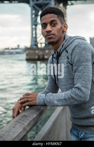 Ein junger Mann sitzt und den Blick auf New Yorks Williamsburg Brücke bewundert. Im Herbst 2016 in Brooklyn, New York City gedreht. Stockfoto