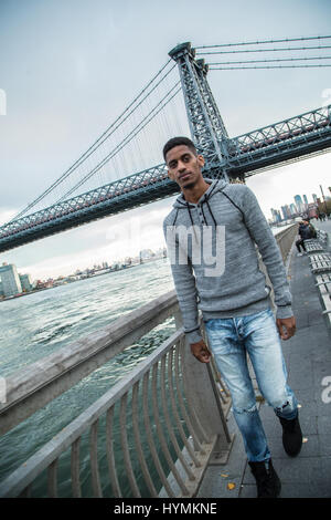 Ein junger Mann sitzt und den Blick auf New Yorks Williamsburg Brücke bewundert. Im Herbst 2016 in Brooklyn, New York City gedreht. Stockfoto