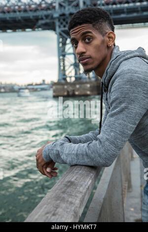 Ein junger Mann sitzt und den Blick auf New Yorks Williamsburg Brücke bewundert. Im Herbst 2016 in Brooklyn, New York City gedreht. Stockfoto