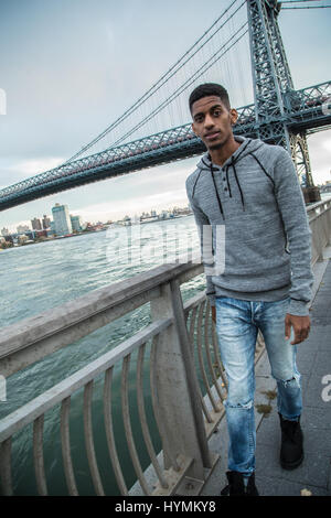 Ein junger Mann sitzt und den Blick auf New Yorks Williamsburg Brücke bewundert. Im Herbst 2016 in Brooklyn, New York City gedreht. Stockfoto