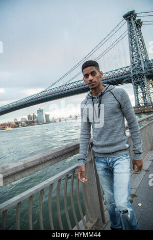 Ein junger Mann sitzt und den Blick auf New Yorks Williamsburg Brücke bewundert. Im Herbst 2016 in Brooklyn, New York City gedreht. Stockfoto