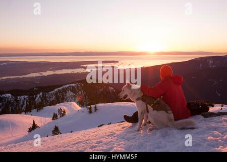 Mann und sein Hund Sonnenuntergang mit Meer Blick vom Gipfel Berges in der Winterzeit, Vancouver, Mount Seymour, British Columbia, Kanada Stockfoto