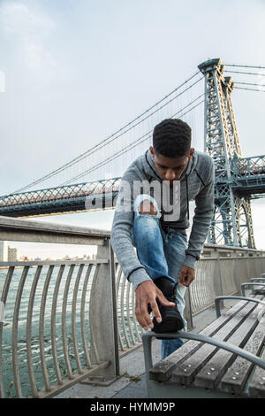 Ehrliches Porträt eines jungen Mannes, der seine Schuhe vor der New Yorker Stadtteil Williamsburg Bridge Reinigung. Gedreht im Herbst 2016. Stockfoto