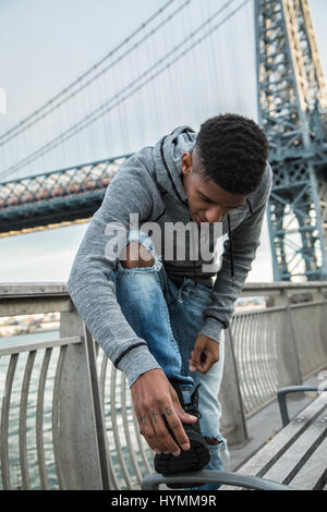 Ein junger Mann sitzt und den Blick auf New Yorks Williamsburg Brücke bewundert. Im Herbst 2016 in Brooklyn, New York City gedreht. Stockfoto