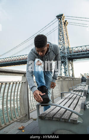 Ein Porträt von einem jungen, schwarzen Mann, sinnend stehen entlang der New Yorker East River und Williamsburg Bridge. Stockfoto