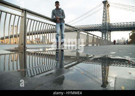 Ein junger Mann sitzt und den Blick auf New Yorks Williamsburg Brücke bewundert. Im Herbst 2016 in Brooklyn, New York City gedreht. Stockfoto