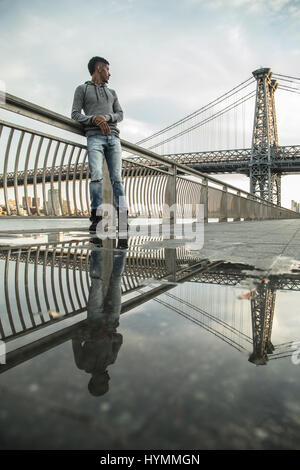 Ein junger Mann sitzt und den Blick auf New Yorks Williamsburg Brücke bewundert. Im Herbst 2016 in Brooklyn, New York City gedreht. Stockfoto