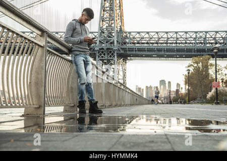 Ein junger Mann sitzt und den Blick auf New Yorks Williamsburg Brücke bewundert. Im Herbst 2016 in Brooklyn, New York City gedreht. Stockfoto