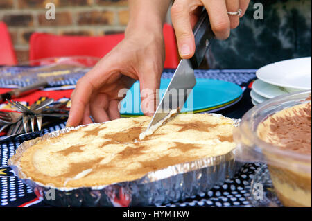 Weibliche Hände slicing hausgemachte Kuchen mit Messer Stockfoto