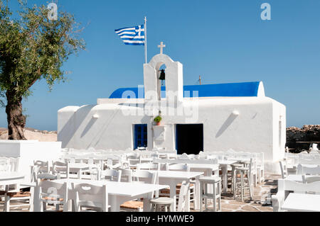 Blick auf die Agios Nikolaos-Kirche in Naoussa, Paros in Griechenland. Vor der Kirche Isa Terrasse mit weißen Tischen und Stühlen. Stockfoto