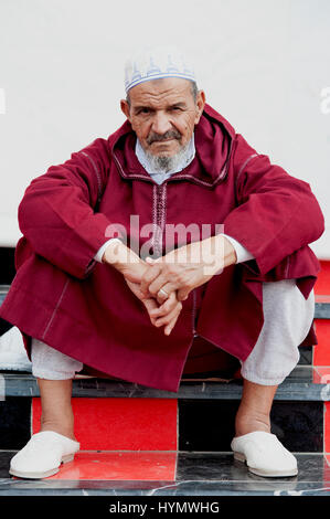 Ältere Menschen muslimischen Mann, Ouarzazate, Marokko, 2016. Ein bärtiger muslimischen Mann sitzen auf rot und schwarz gefliesten Stufen in den wichtigsten Platz von Ouarzazate in Marokko. Stockfoto