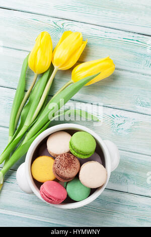 Bunte Makronen Plätzchen und gelbe Tulpen Strauß auf Holztisch. Ansicht von oben Stockfoto